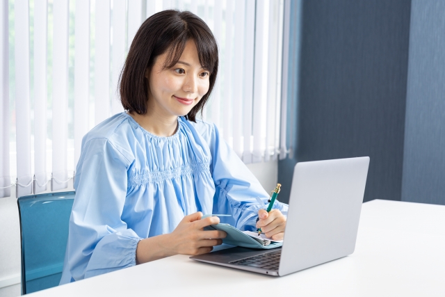 ノートパソコンと手帳を使って在宅ワークをする女性