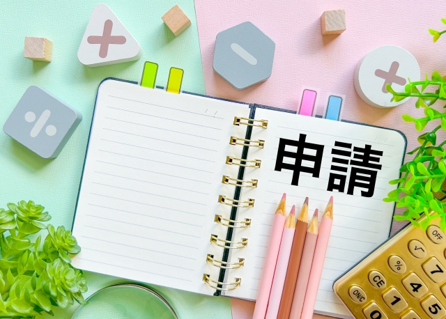 申請の文字とノート、電卓、文房具が並ぶ写真