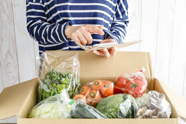 ふるさと納税の返礼品として届いた野菜セットを確認する母子家庭のお母さん。タブレットで寄付の管理をしている様子。