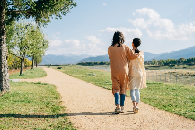 母子家庭の母親と一人っ子の子どもが手をつなぎ、穏やかな道を寄り添って歩く様子。相続や将来への安心をイメージした写真。