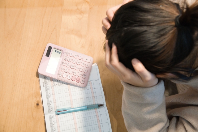 住民税が非課税から課税になり、家計の負担や支援の変化に不安を感じている母子家庭のお母さんが家計簿と電卓を前に頭を抱えている様子